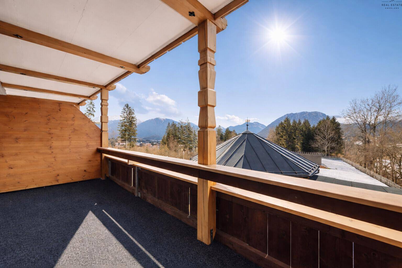 Sonniger Balkon mit weitem Blick auf die umliegende Berglandschaft und blauen Himmel.