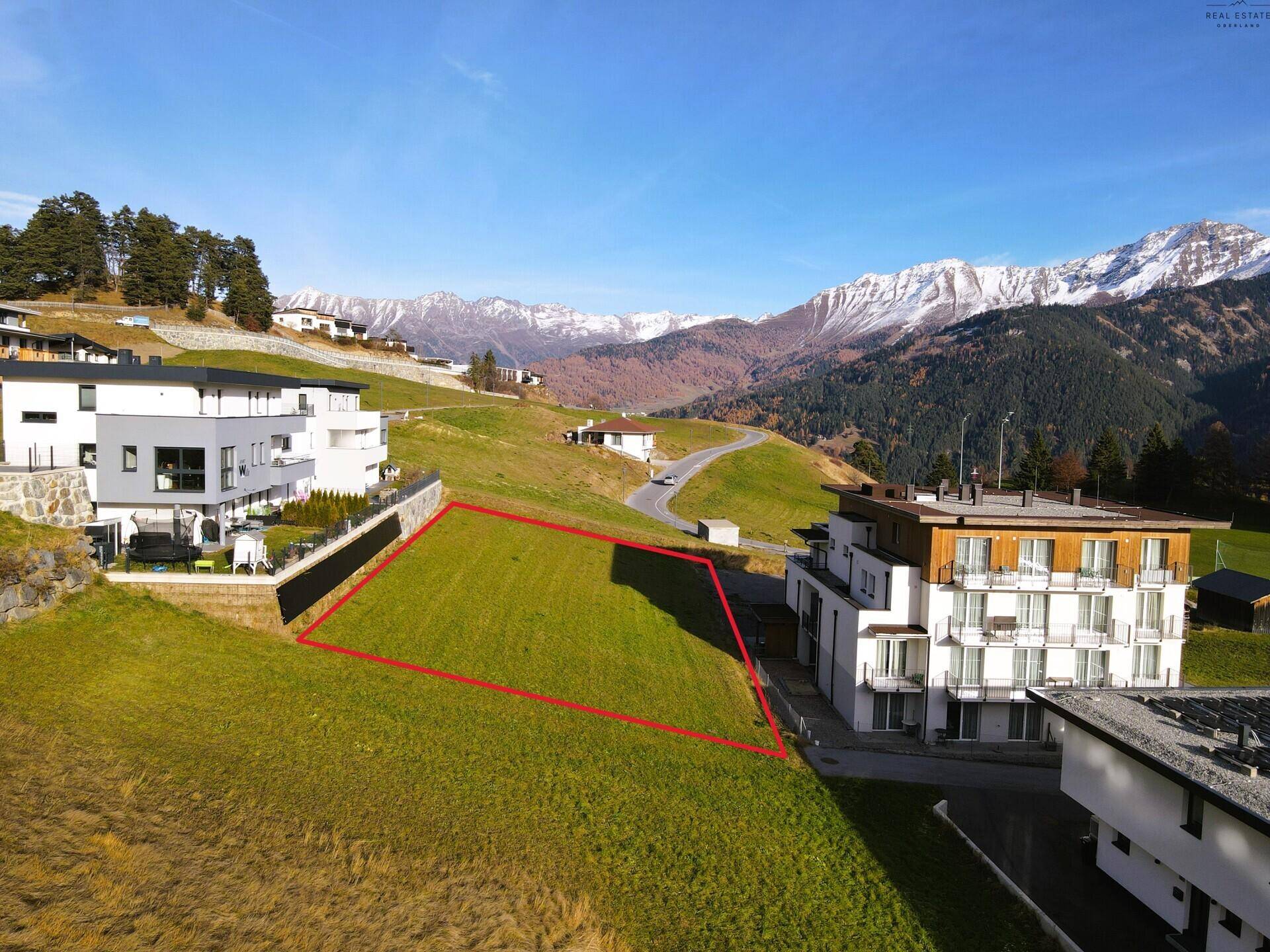 Luftaufnahme eines Baugrundstücks mit roter Umrandung inmitten einer Berglandschaft.