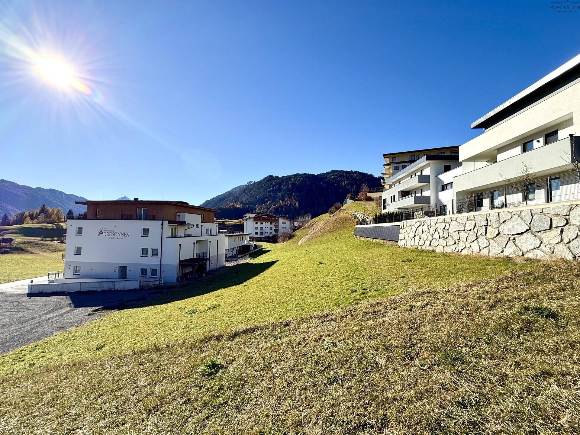 Gebäudekomplex mit moderner Architektur in sonniger alpiner Umgebung und Bergblick.