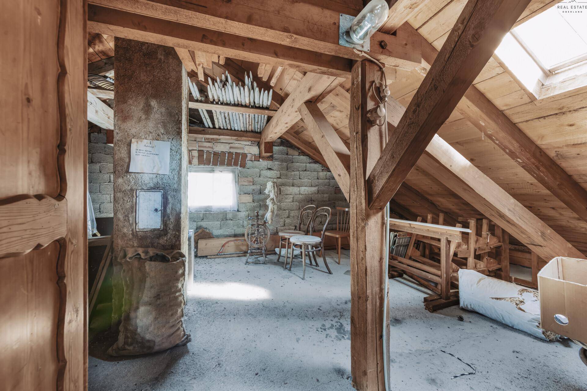 Dachboden mit sichtbaren Holzbalken, Ziegelwänden und Dachfenster.