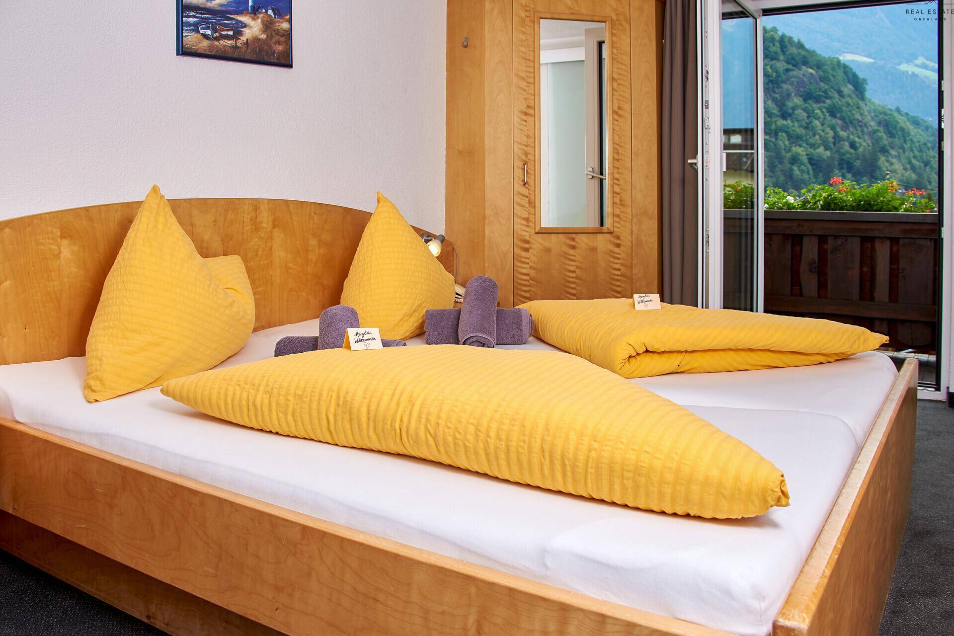 Schlafzimmer mit Doppelbett, gelber Bettwäsche und Zugang zu einem Balkon mit Bergblick.