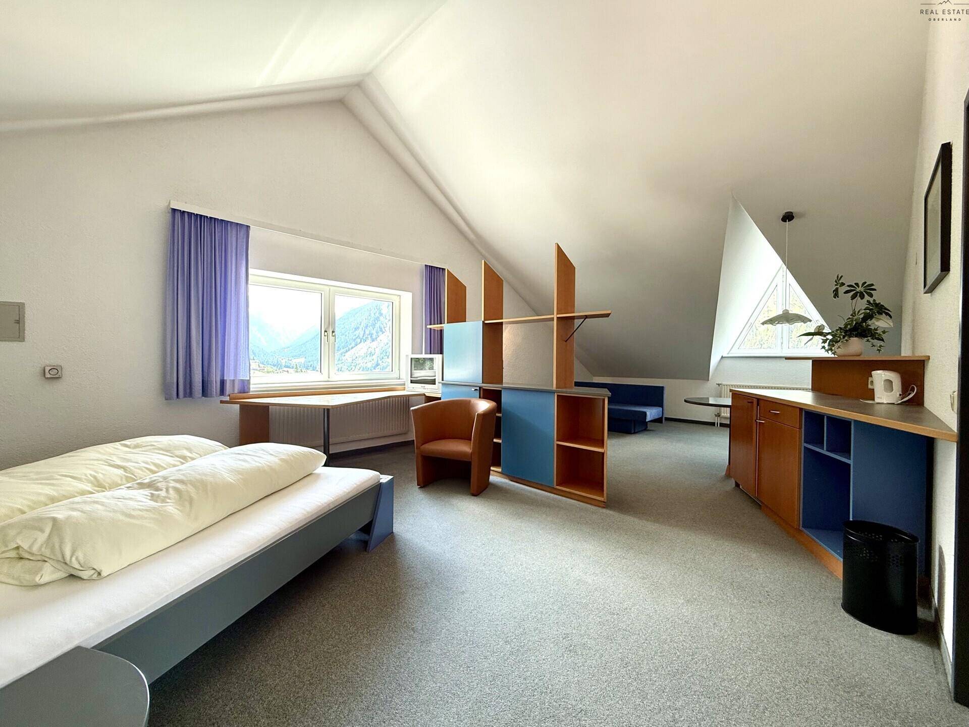 Geräumiges Schlafzimmer mit Teppichboden, Bett und einem Schreibtischbereich unter dem Fenster.