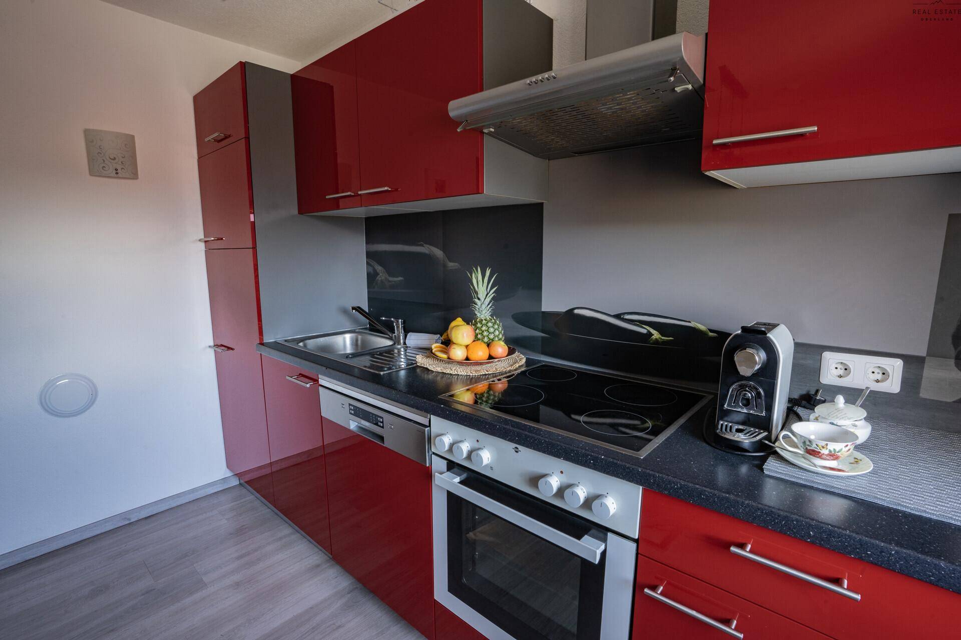 Detailansicht der modernen roten Küche mit Kochfeld, Backofen, Spüle und Kaffeemaschine.