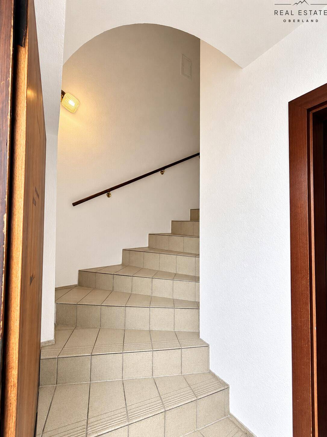 Treppenhaus mit gefliesten Stufen und Holzgeländer, das in die oberen Stockwerke führt.
