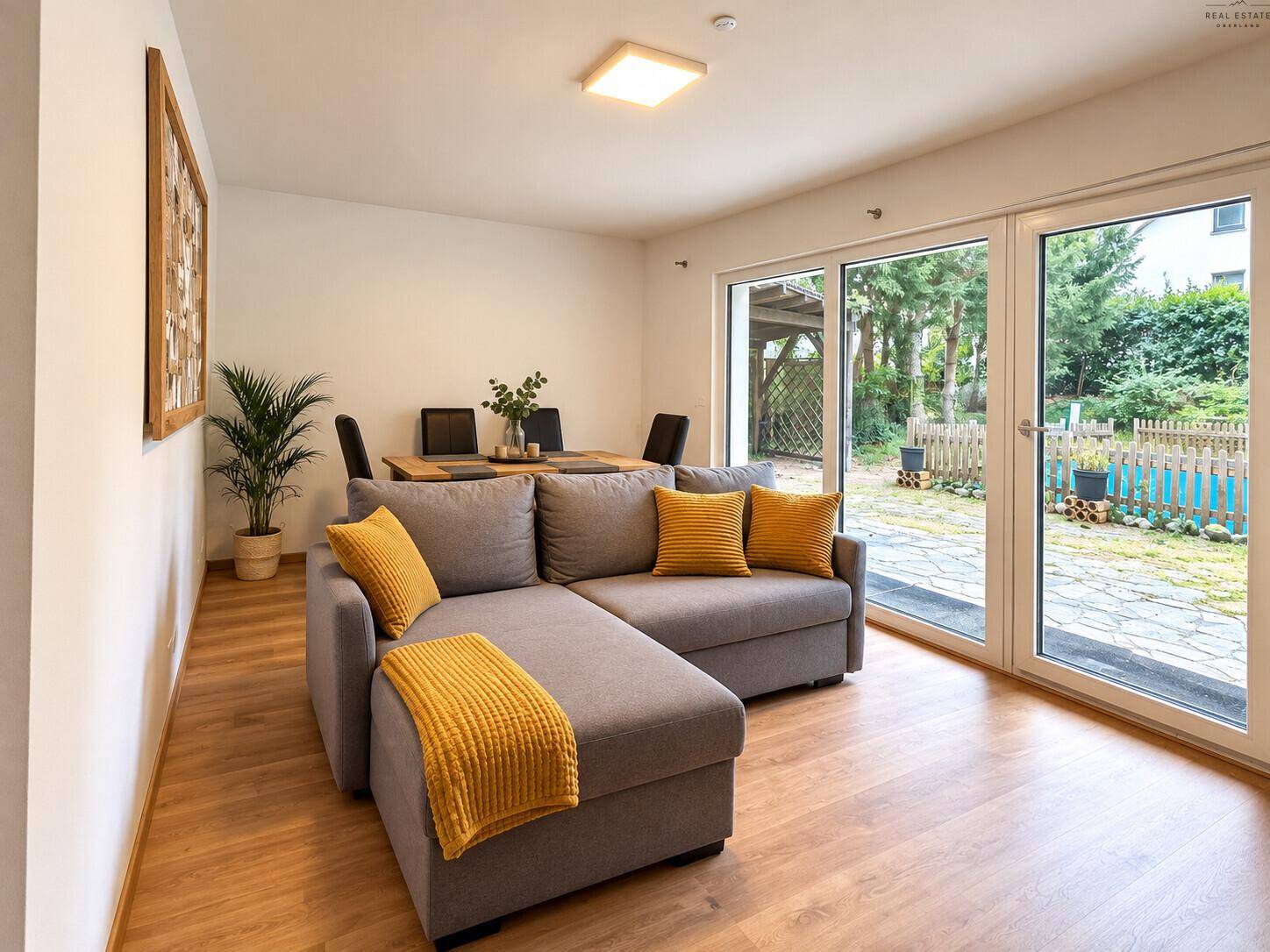 Heller Wohn- und Essbereich mit bequemer Couch, Holzboden und Zugang zum Garten.