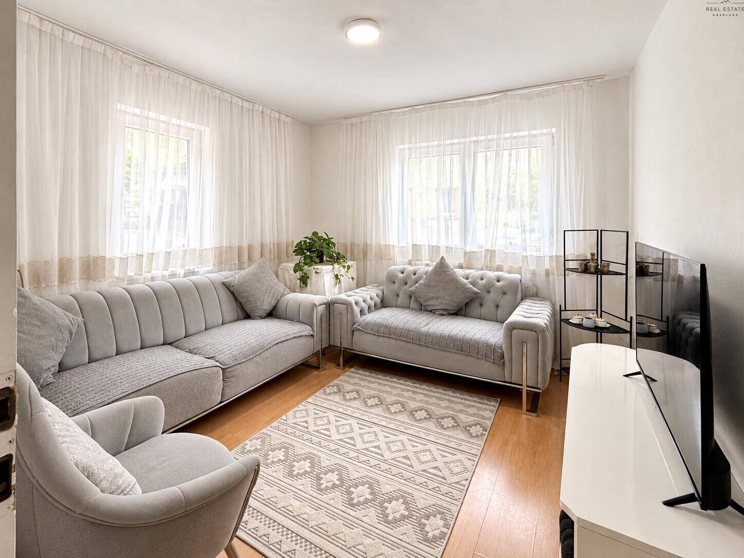 Stilvolles Wohnzimmer mit bequemen Sitzmöbeln, Teppich und viel Tageslicht durch große Fenster.