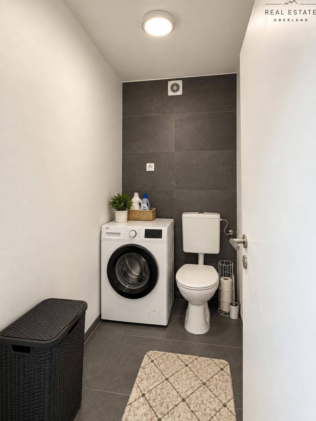 Modernes Gäste-WC mit dunklen Fliesen, Toilette und integrierter Waschmaschine.