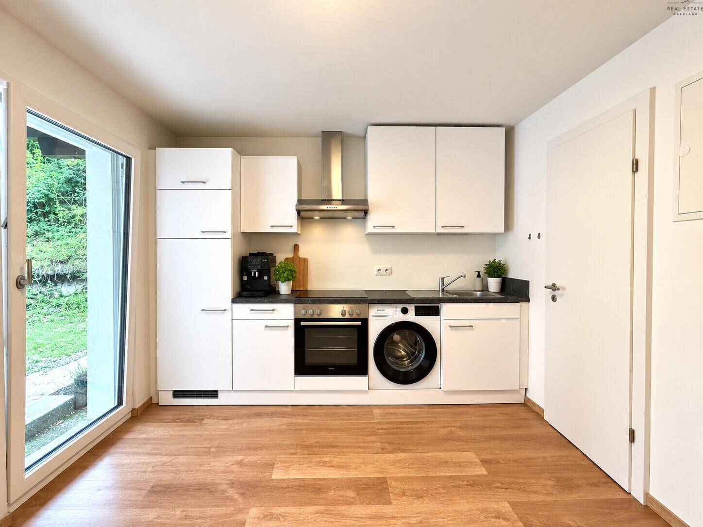 Moderne Einbauküche in Weiß mit integrierter Waschmaschine und Zugang zum Garten.