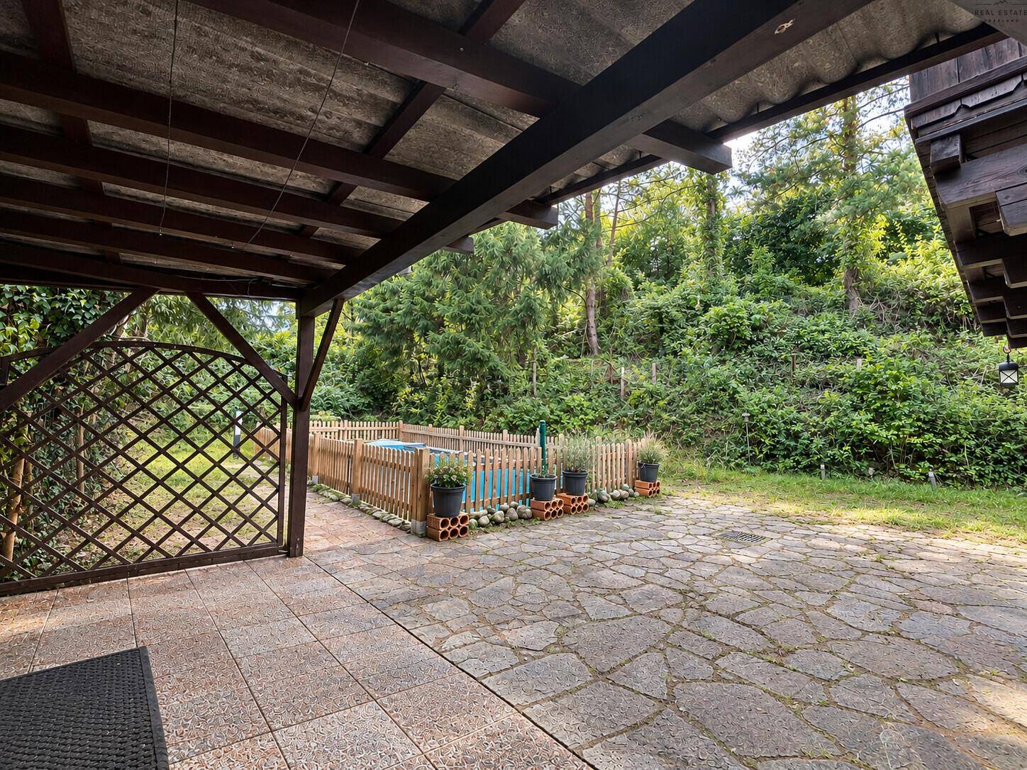 Überdachte Terrasse mit Steinplatten, kleinem Pool und umgebender grüner Vegetation.