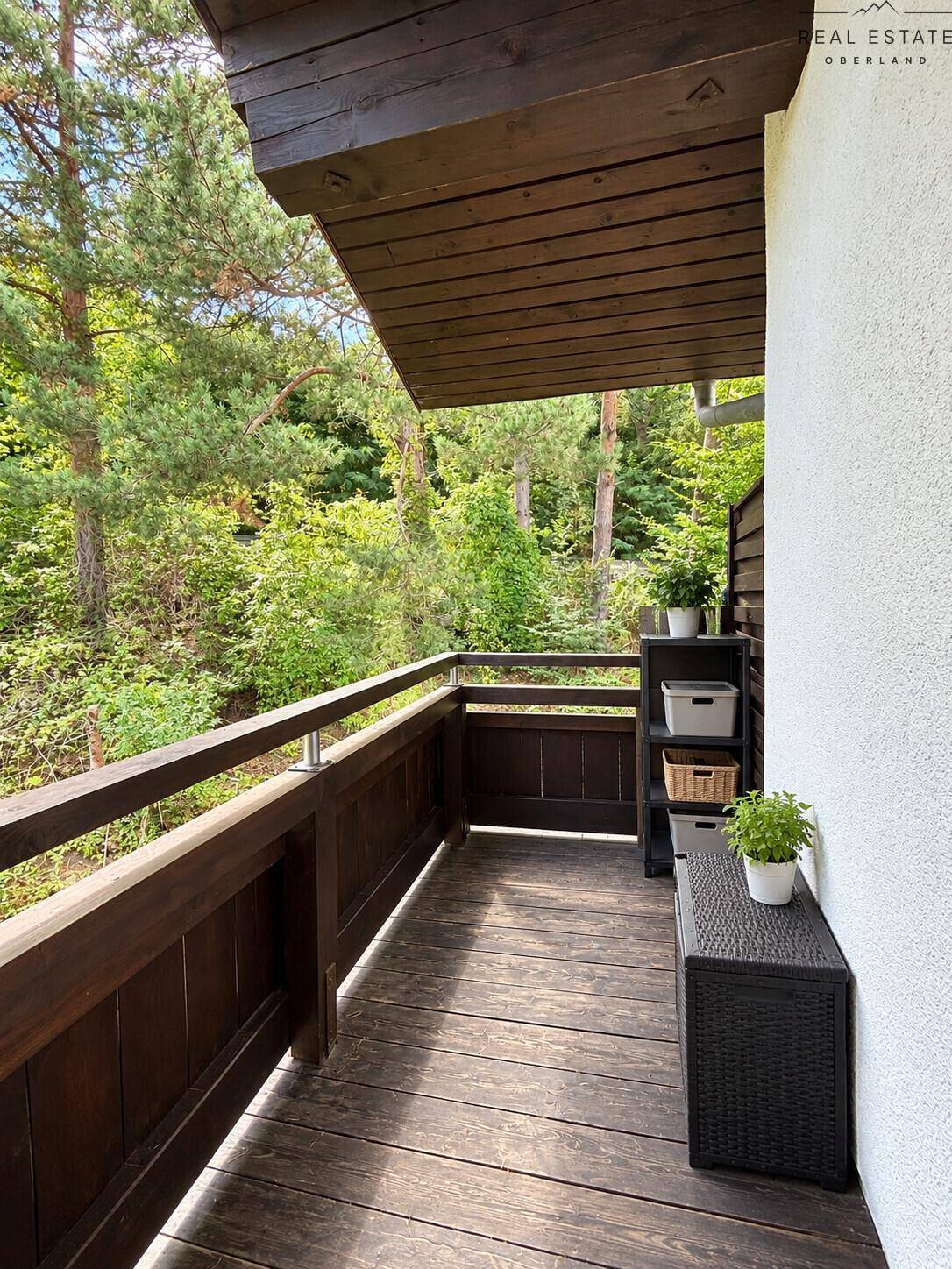 Balkon mit Holzboden und Blick ins Grüne, umgeben von Bäumen.