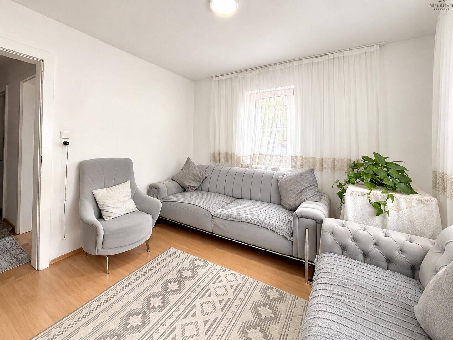 Elegantes Wohnzimmer mit zwei grauen Sofas, Teppich und hellen Vorhängen an den Fenstern.