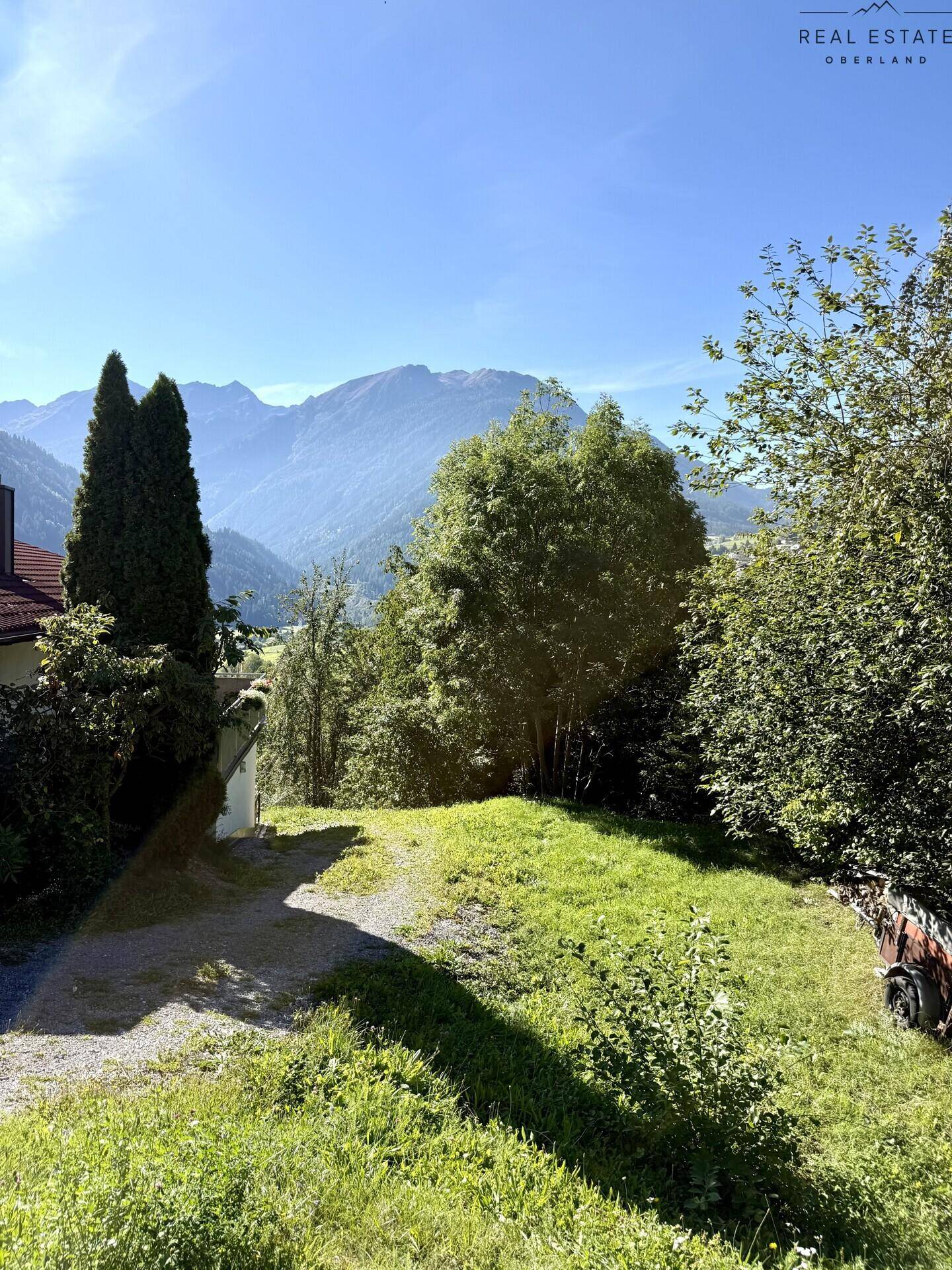 Zufahrt zu einem Grundstück mit grüner Umgebung und Bergblick im Hintergrund.