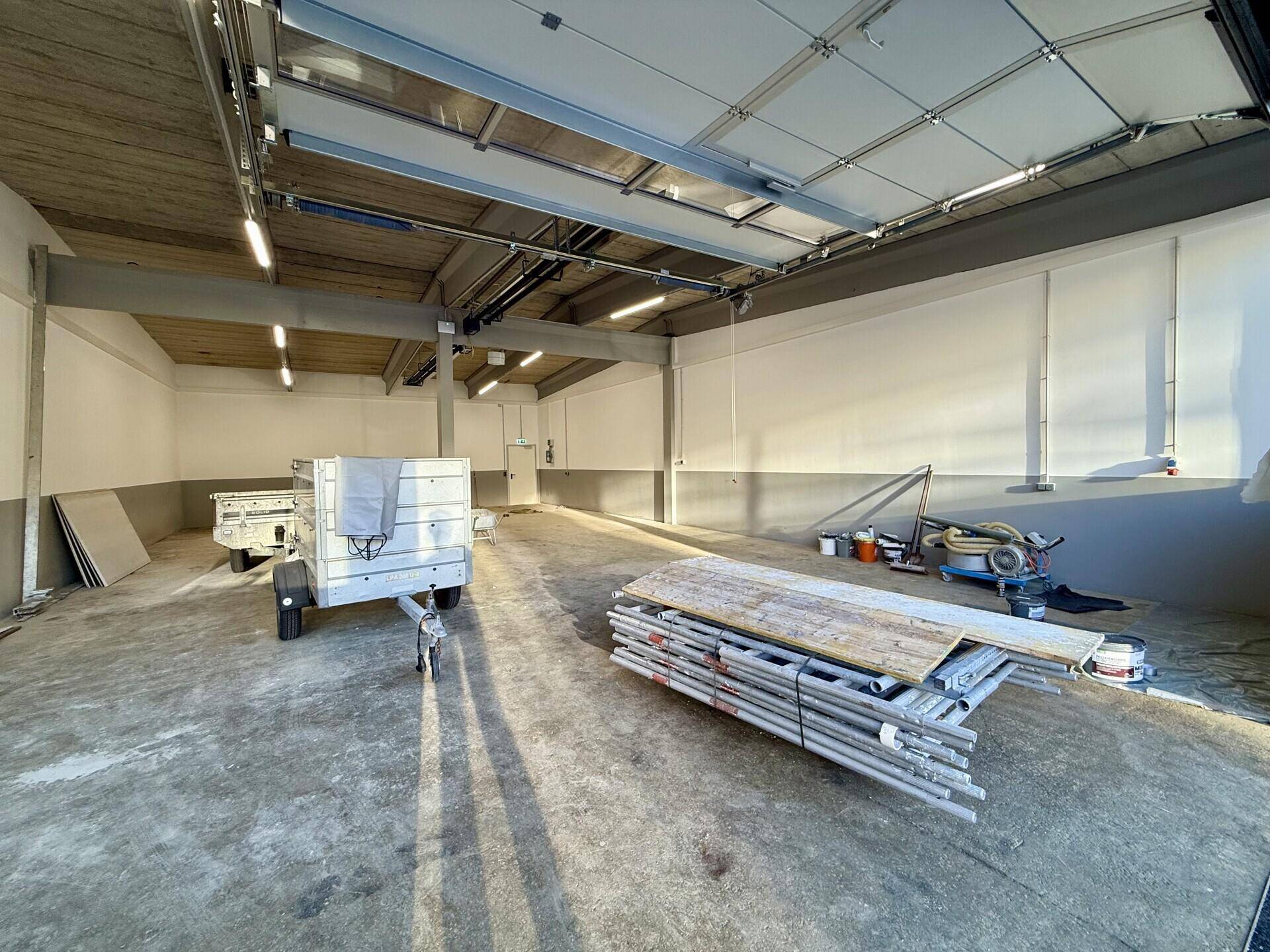Weitläufiger Innenraum einer Halle mit Betonboden, sichtbaren Trägern und Deckenbeleuchtung.