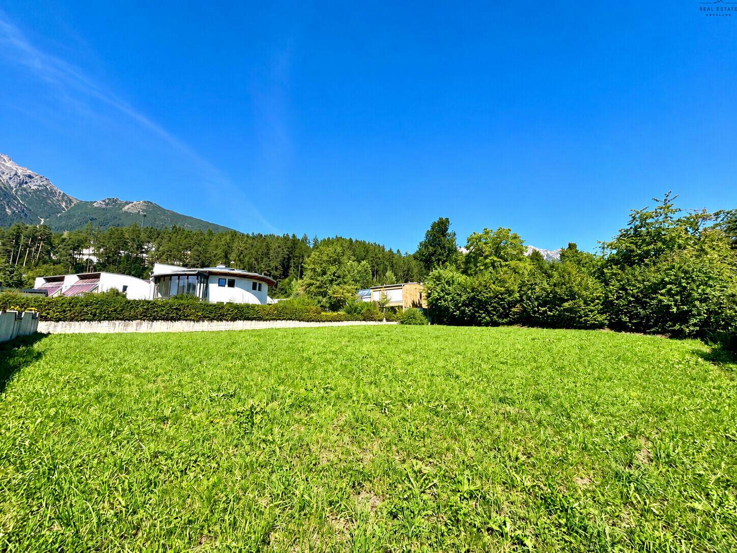 Sonnige Wiese mit Blick auf die Berge und weitere Gebäude in der Ferne.