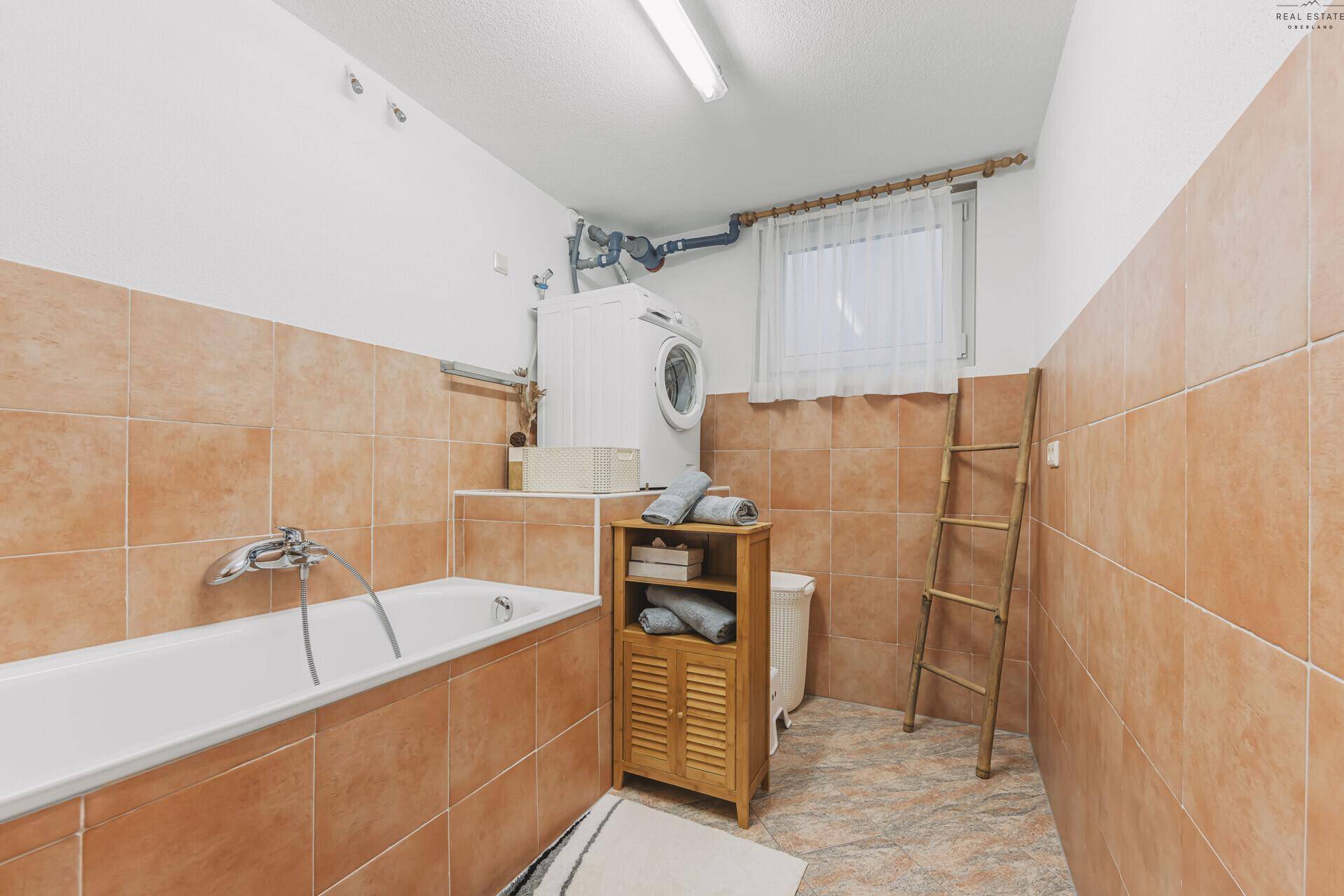 Funktionales Badezimmer mit Badewanne, Waschmaschine und braunen Wandfliesen.