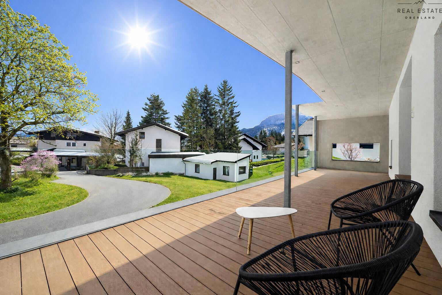 Sonniger Balkon mit bequemen Sitzgelegenheiten, Holzboden und beeindruckendem Panoramablick auf die Berge.