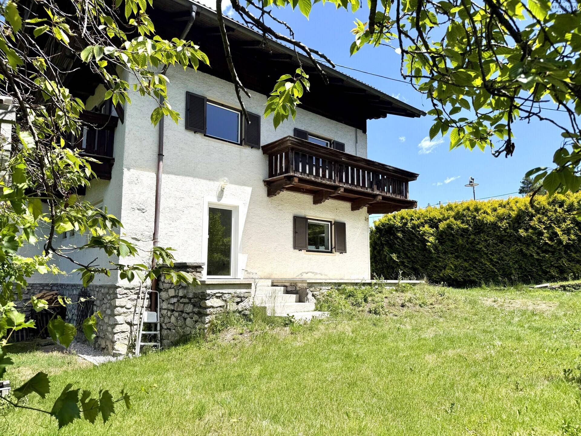 Traditionelles Haus mit Holzbalkon und grüner Hecke im Vordergrund.
