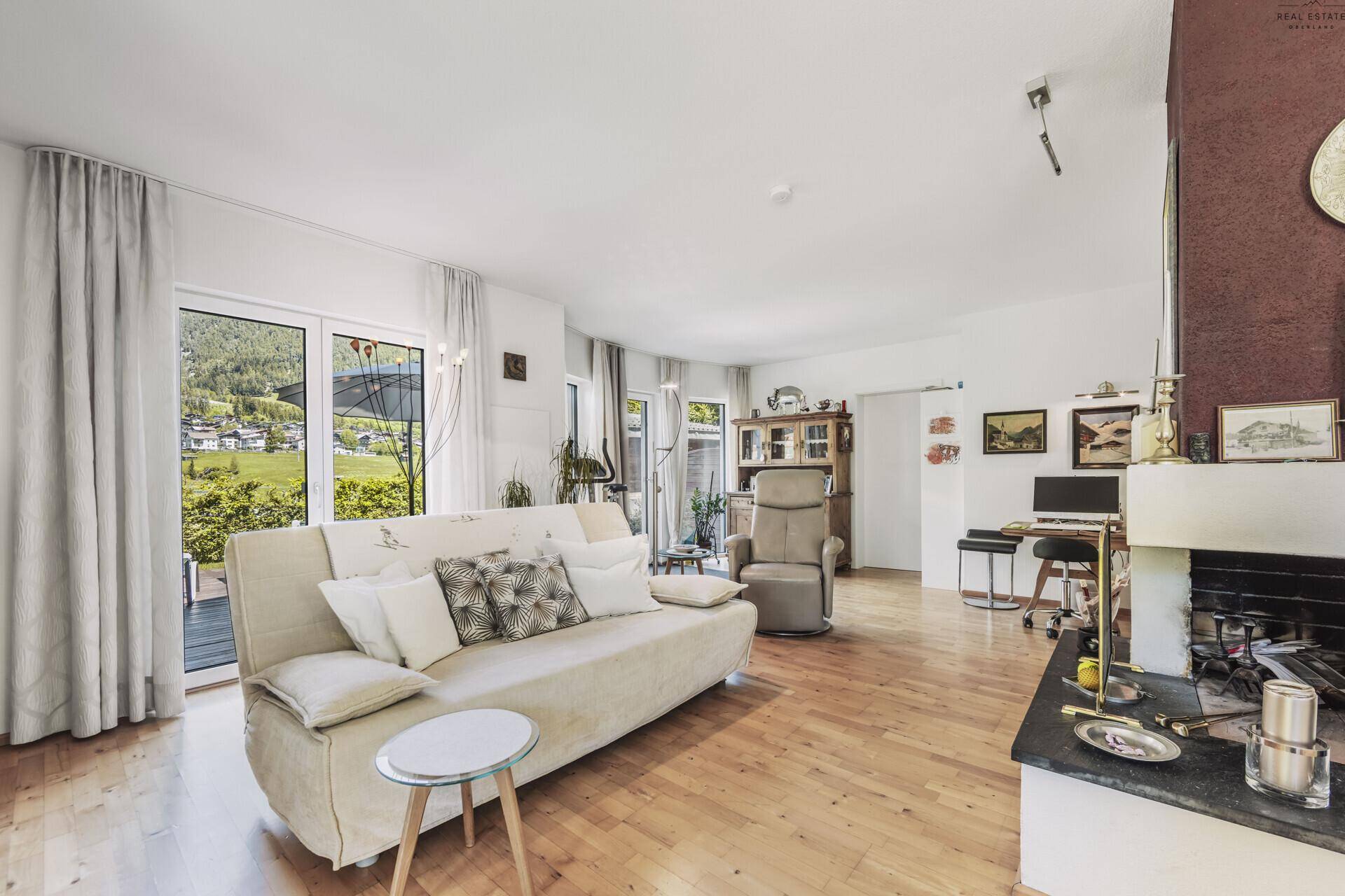 Helles Wohnzimmer mit gemütlichem Sofa, Kamin und großen Fenstern mit Bergblick.