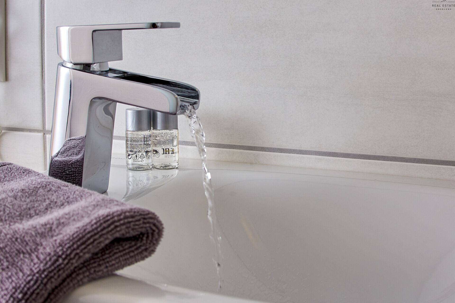 Nahaufnahme eines modernen Wasserhahns mit fließendem Wasser über einem weißen Waschbecken.