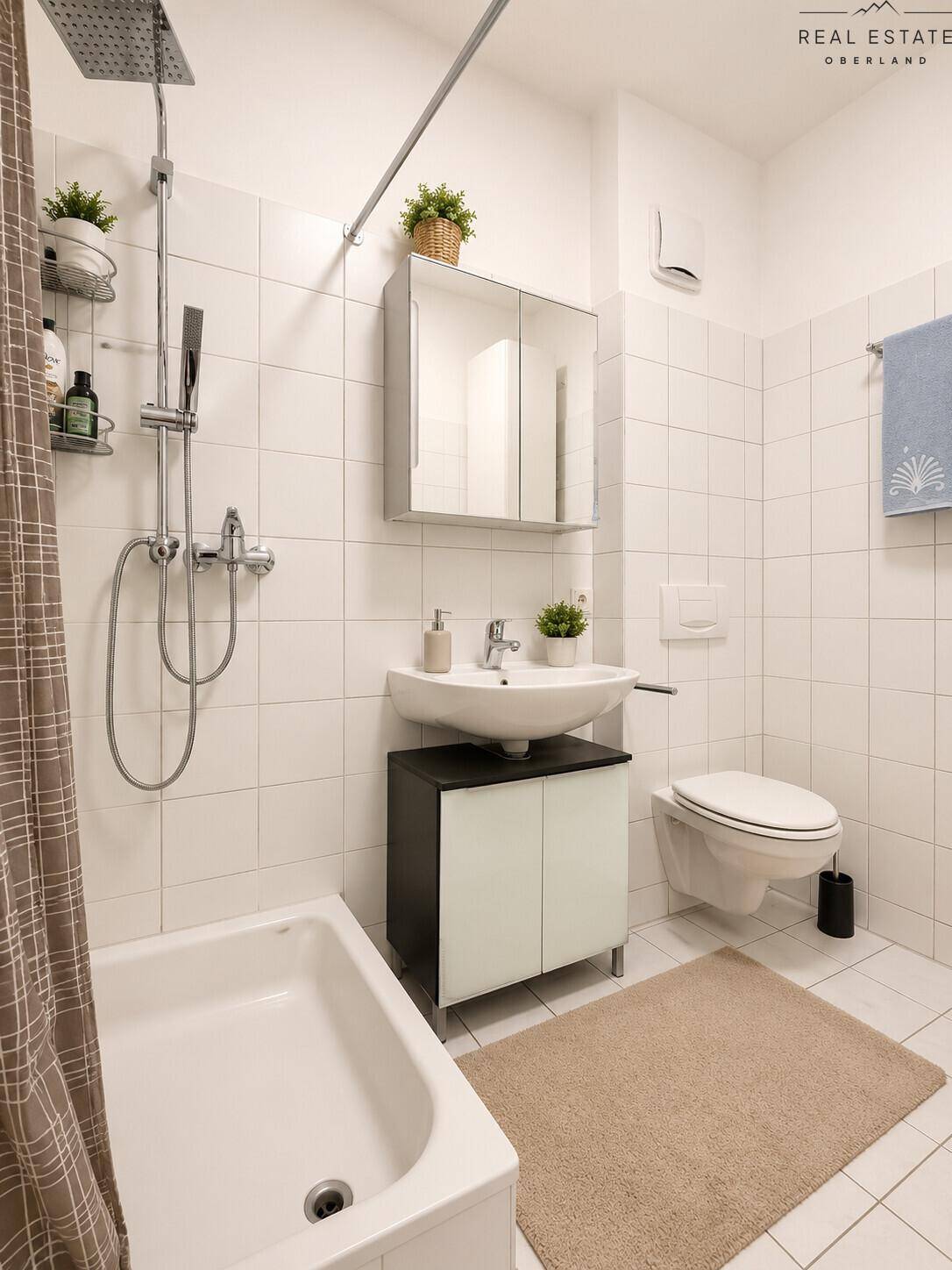 Helles Badezimmer mit weißen Fliesen, Badewanne mit Duschfunktion und modernem Waschtisch.