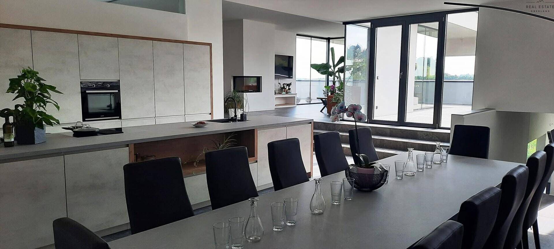 Moderner Küchen- und Essbereich mit langem Tisch, Einbaugeräten und großen Fenstern, die viel Licht hereinlassen.