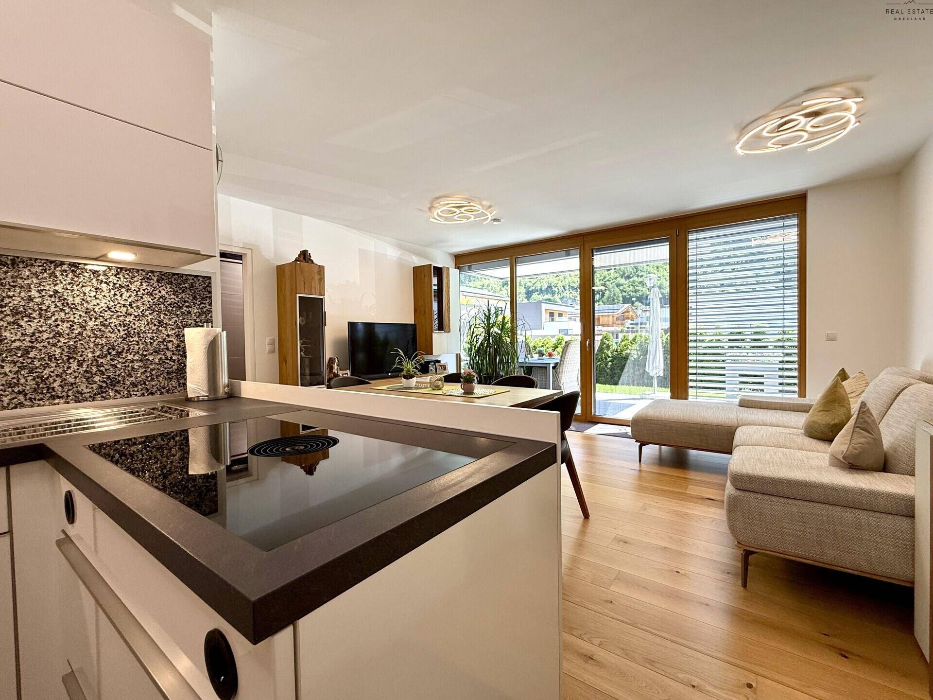 Offener Wohnbereich mit Induktionskochfeld, Sofa und großen Fenstern mit Zugang zur Terrasse.