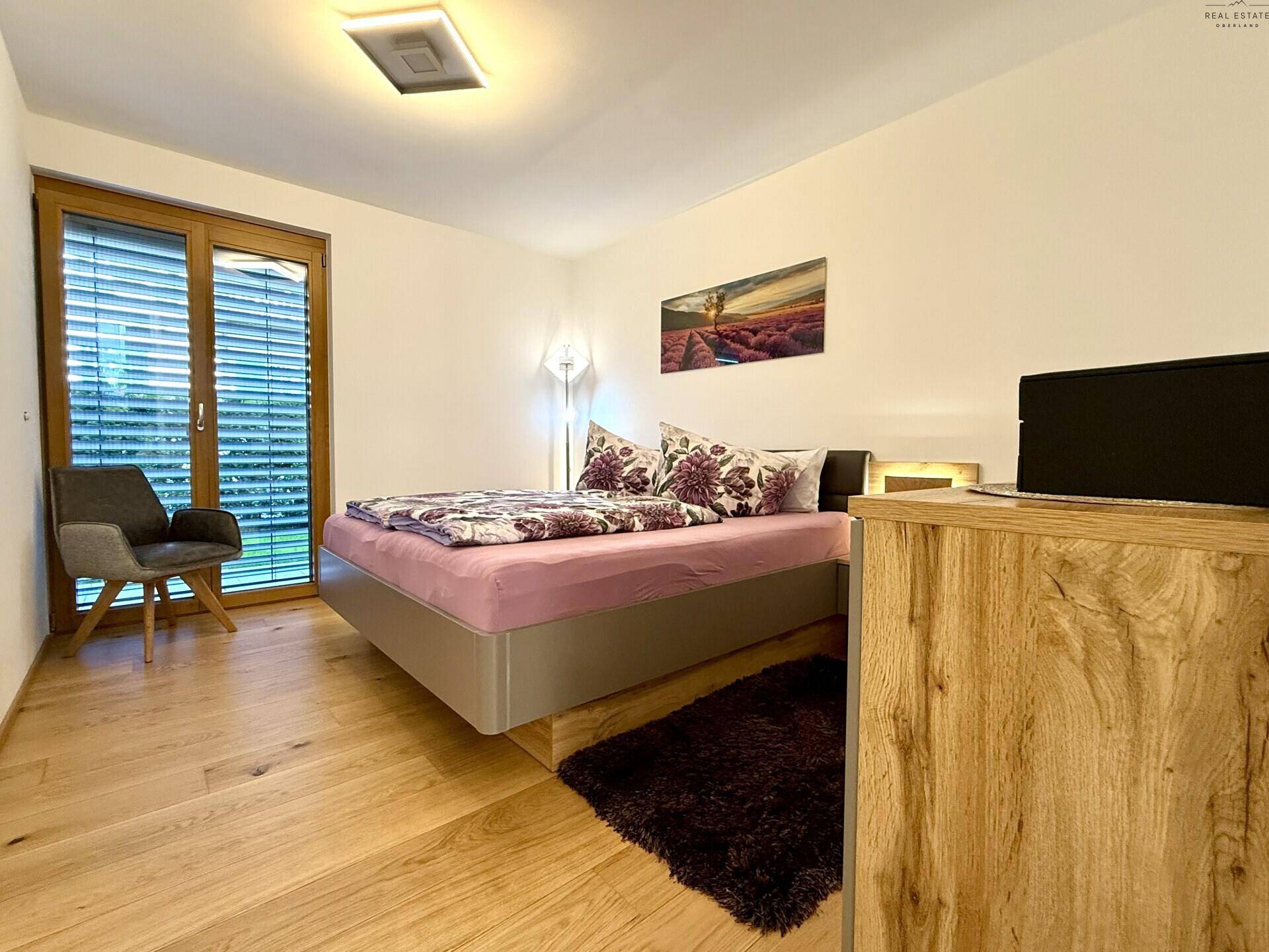Helles Schlafzimmer mit Holzboden, großem Fenster und moderner Kommode.