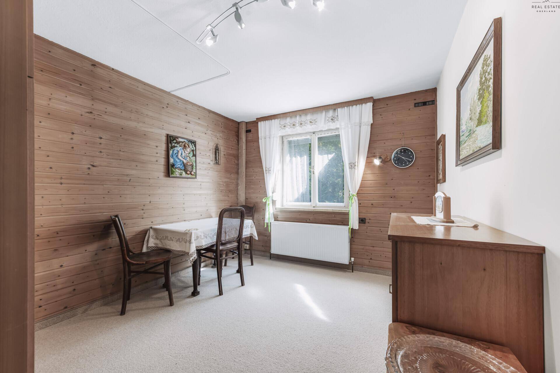 Helles Zimmer mit Holzvertäfelung, Esstisch und Stühlen, durch Fenster gut belichtet.