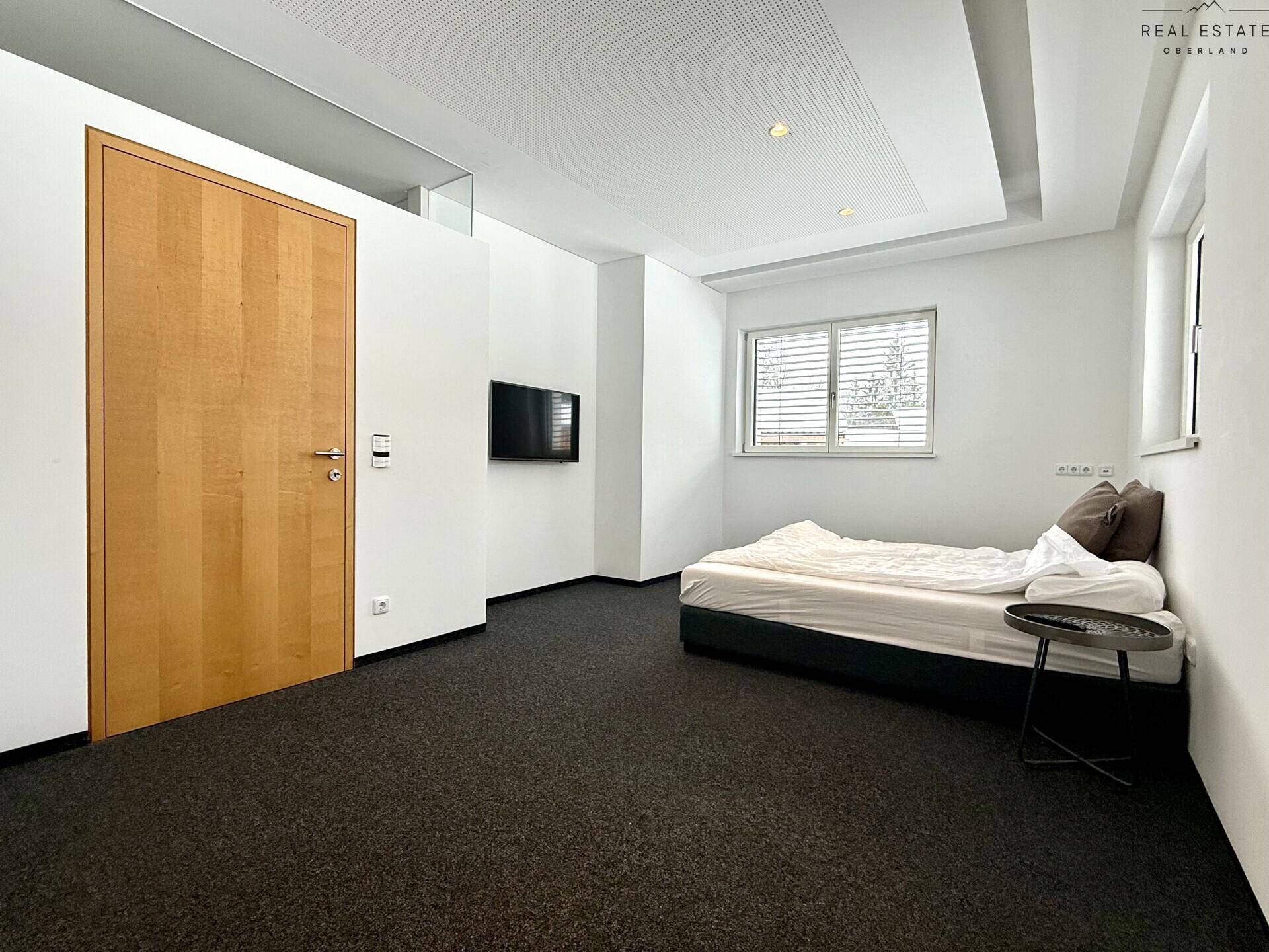Gemütliches Schlafzimmer mit dunklem Teppichboden, einem Bett und Fenster für natürliches Licht.