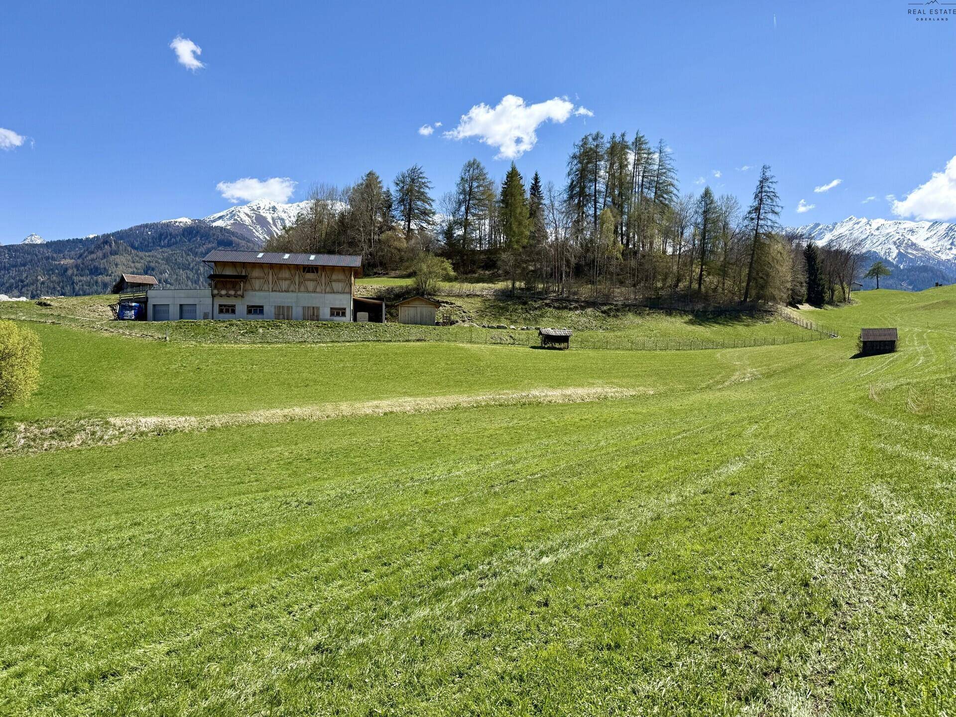 Großzügige grüne Landschaft mit einem modernen Haus, umgeben von Bäumen und einer beeindruckenden Bergkulisse.