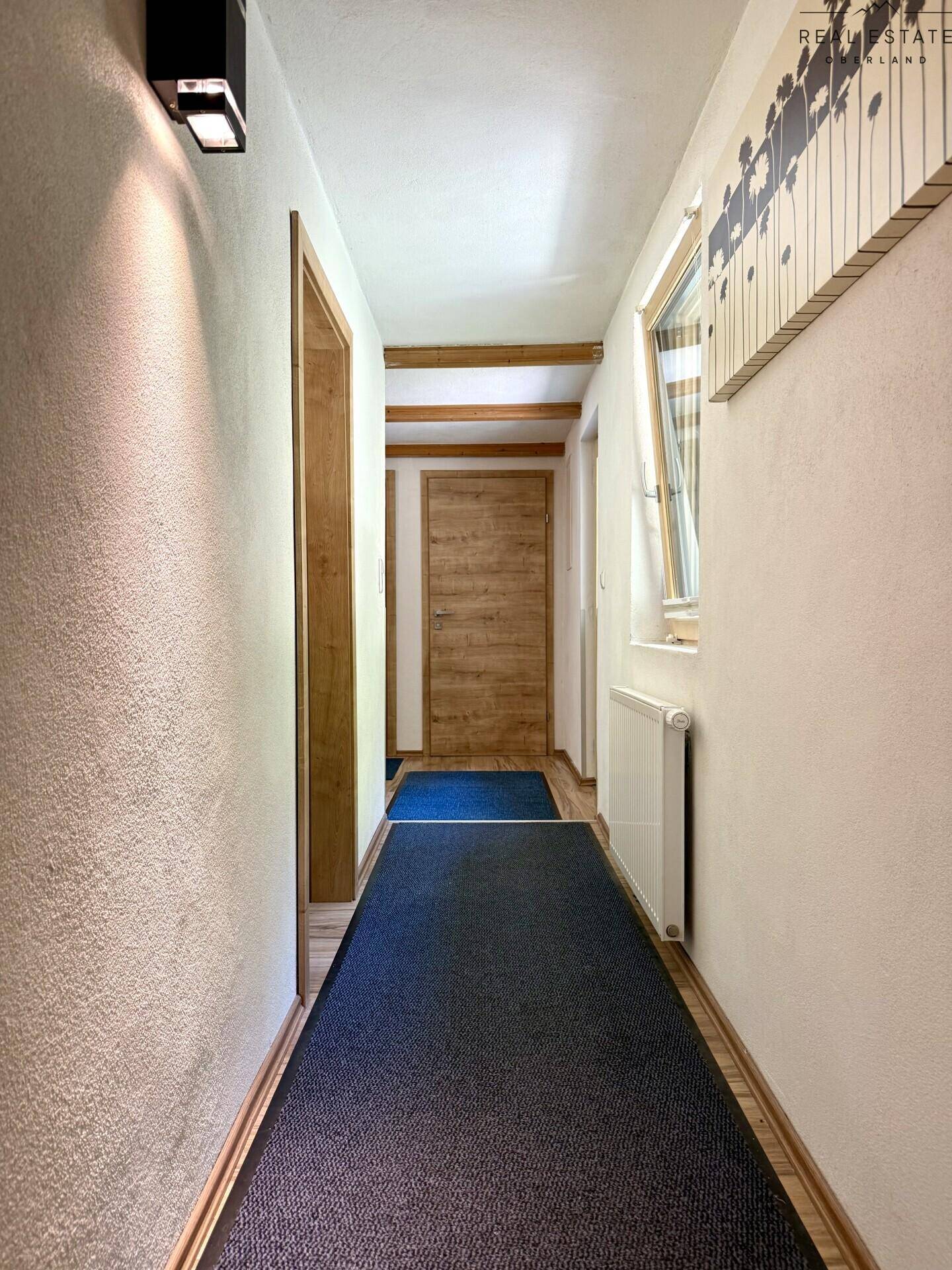 Langer Flur mit Holztüren, Teppichläufer und sichtbaren Holzbalken an der Decke.