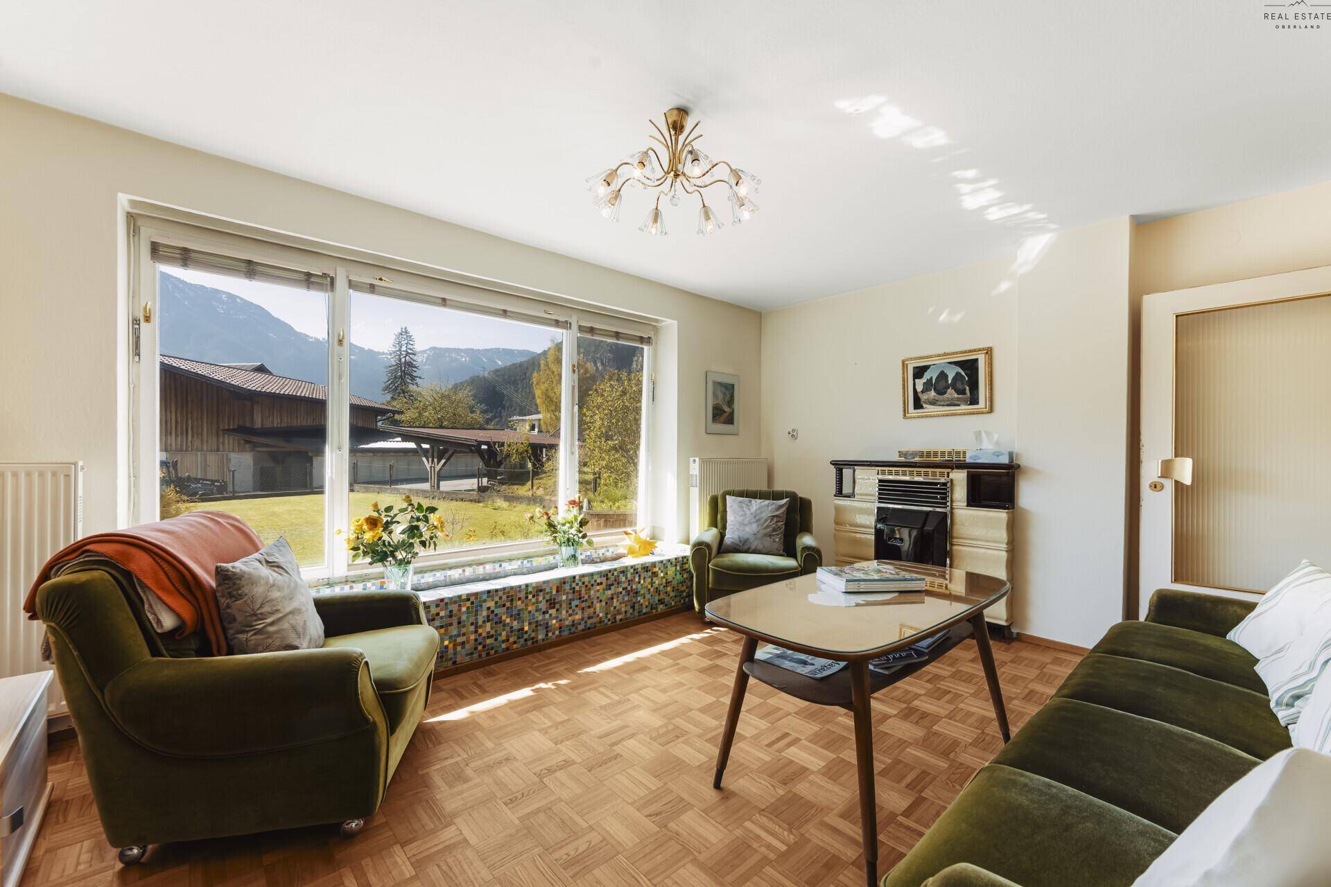 Helles Wohnzimmer mit Parkettboden, gemütlichen Sesseln und Bergblick durch große Fenster.