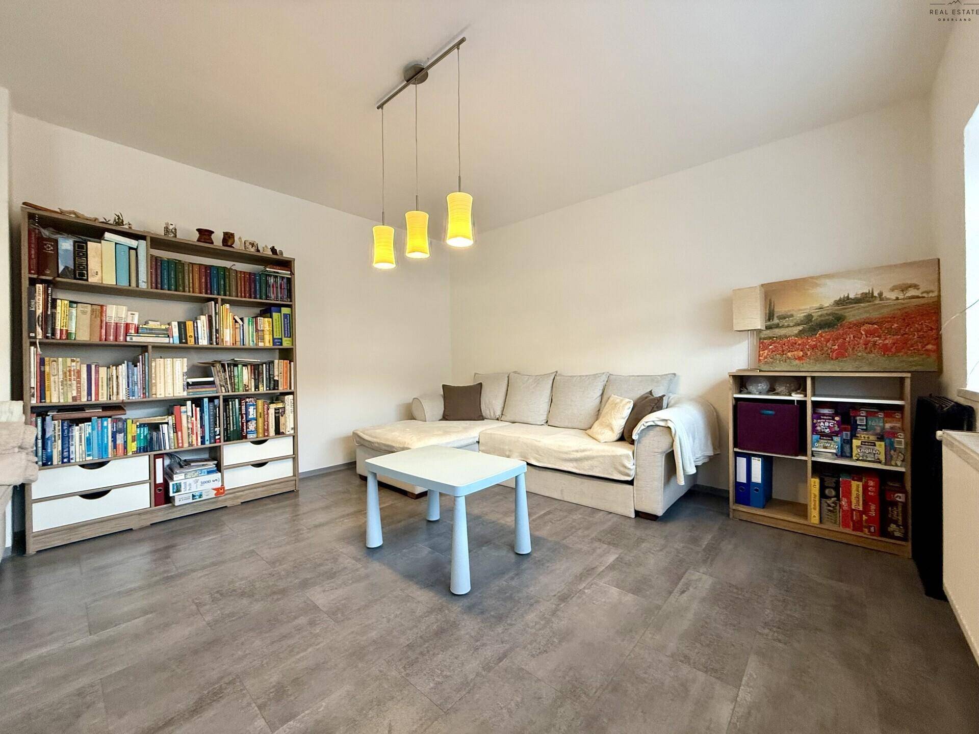 Gemütliches Wohnzimmer mit Sofa, Bücherregal und modernem Laminatboden.