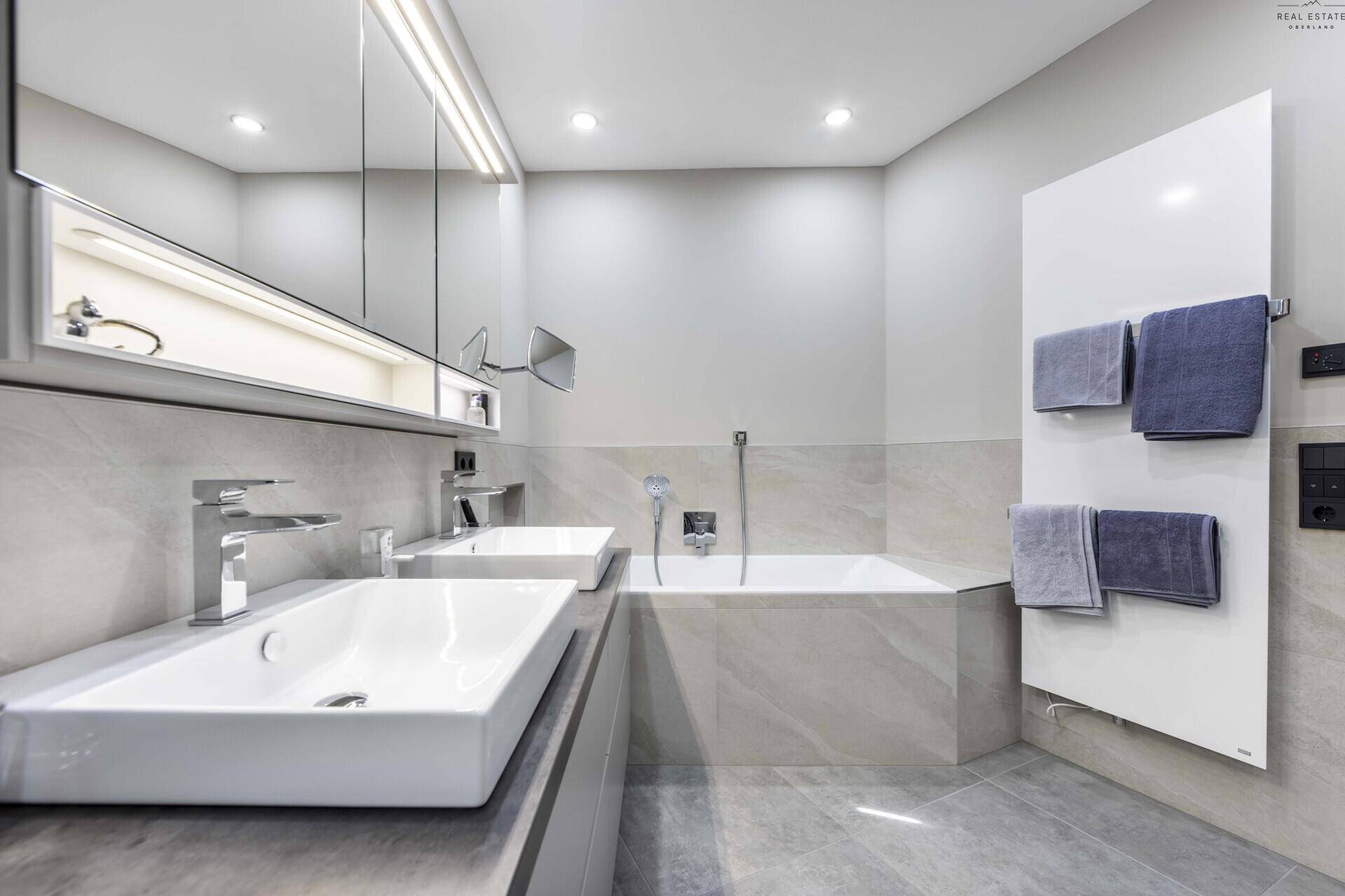 Detailansicht des modernen Badezimmers mit Doppelwaschbecken, Badewanne und beheiztem Handtuchhalter.