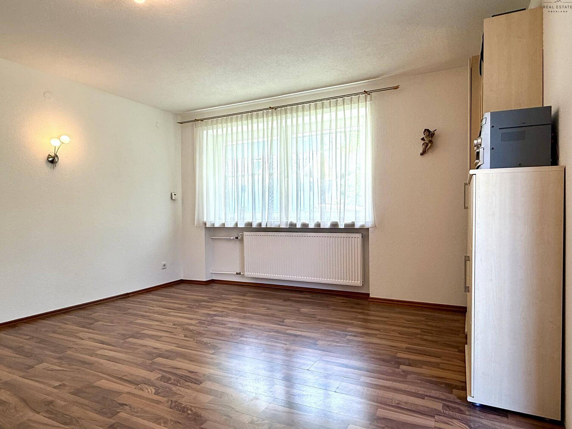 Helles Wohnzimmer mit Laminatboden, großem Fenster und Heizkörper, bietet viel Tageslicht.