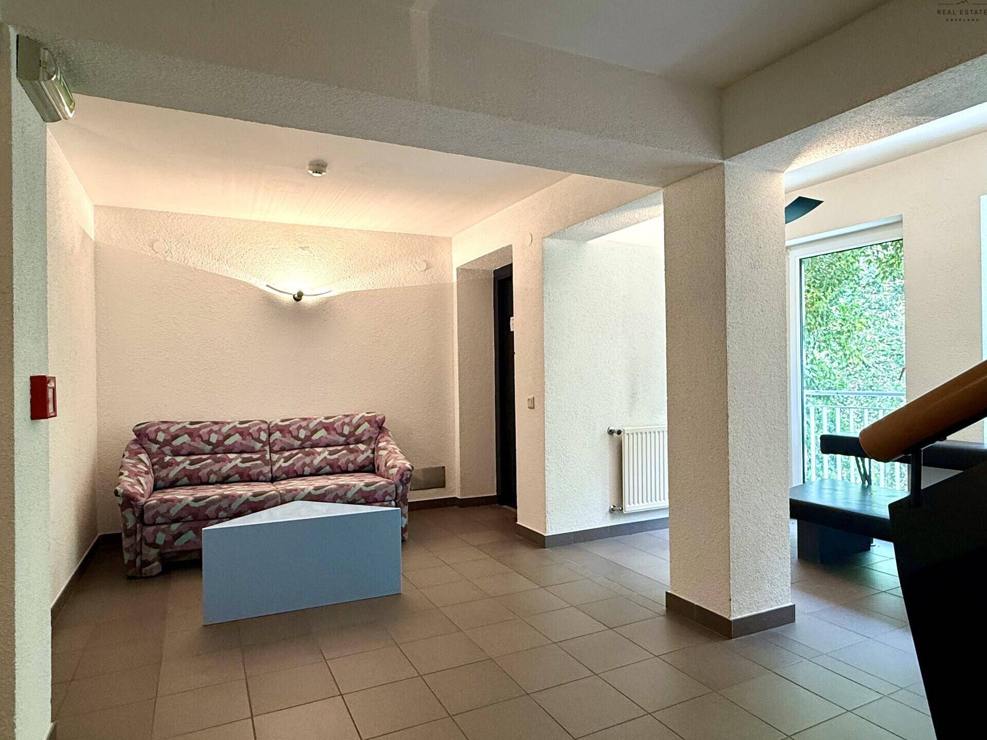 Gemeinschaftsbereich mit Sofa, Fliesenboden und Zugang zu einem Außenbereich.