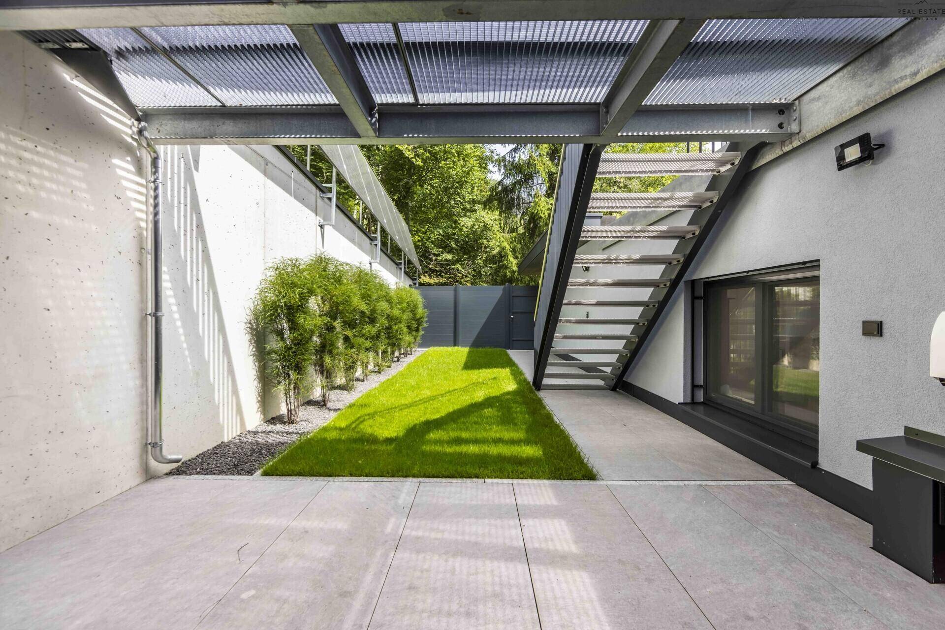 Kleiner, gepflegter Gartenbereich mit Rasenfläche und Hecke unter einer überdachten Struktur.