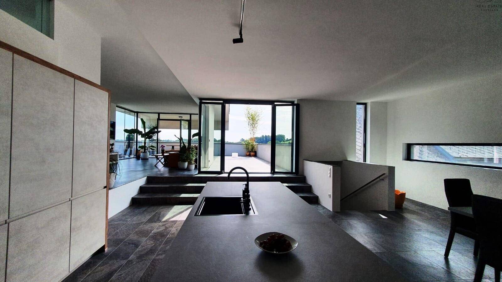 Moderne Küche mit Kochinsel, dunklem Fliesenboden und Stufen zum Wohnbereich mit Terrassenzugang.