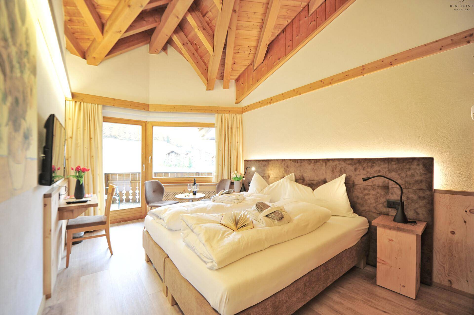 Großzügiges Schlafzimmer mit Doppelbett, sichtbaren Holzbalken und einem Fenster mit schöner Aussicht.