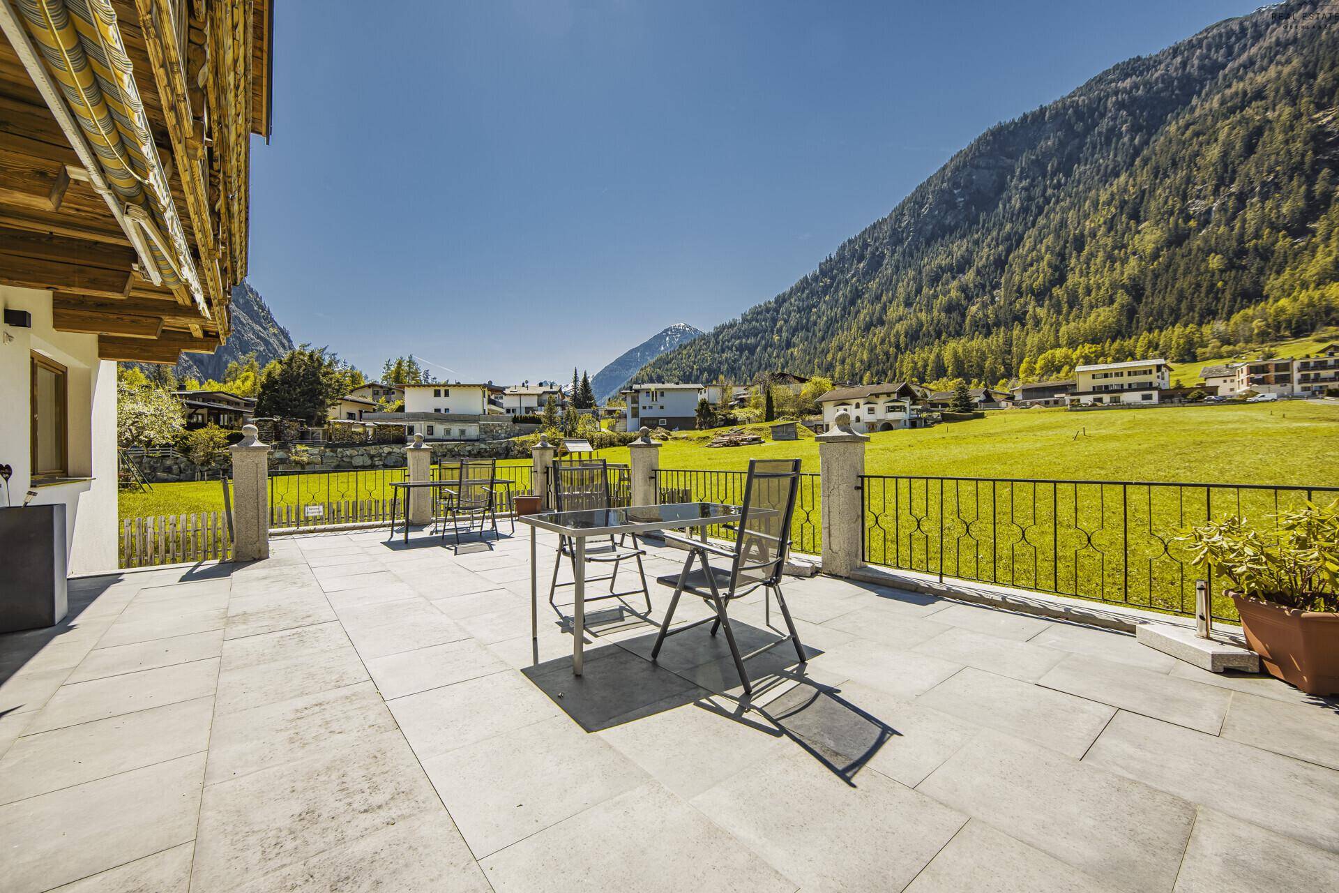 Geräumige Terrasse mit Bergblick und Sitzgelegenheiten, umgeben von grünen Wiesen.