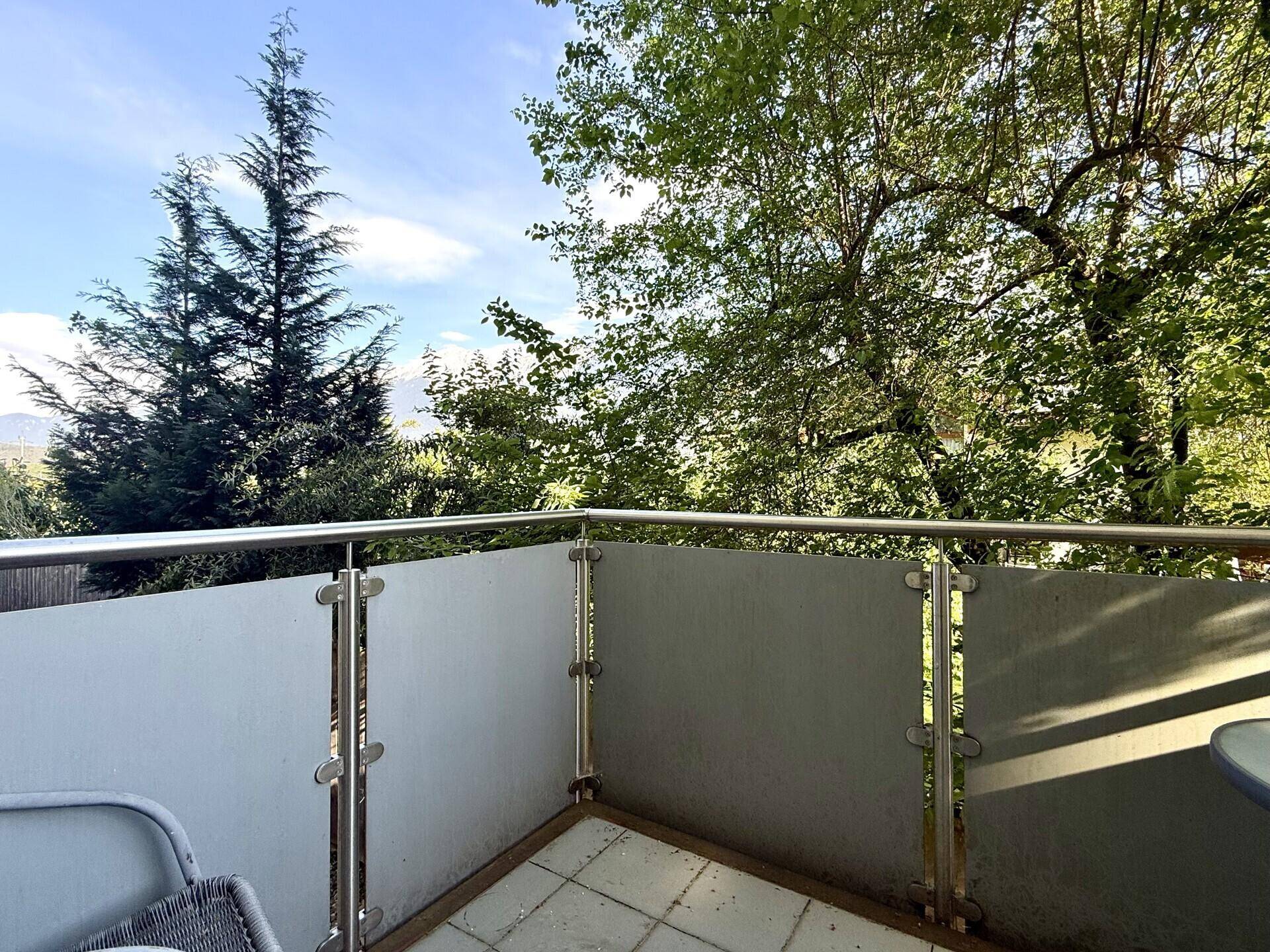 Balkon mit Blick ins Grüne, umgeben von hohen Bäumen und mit Metallgeländer.