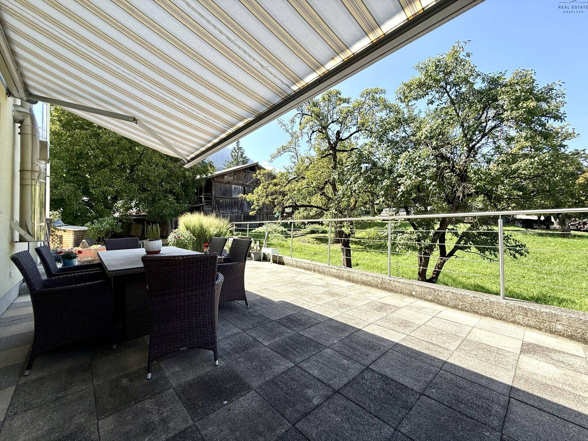 Überdachte Terrasse mit Markise, Gartenmöbeln und weitem Blick ins Grüne und auf die Berge.