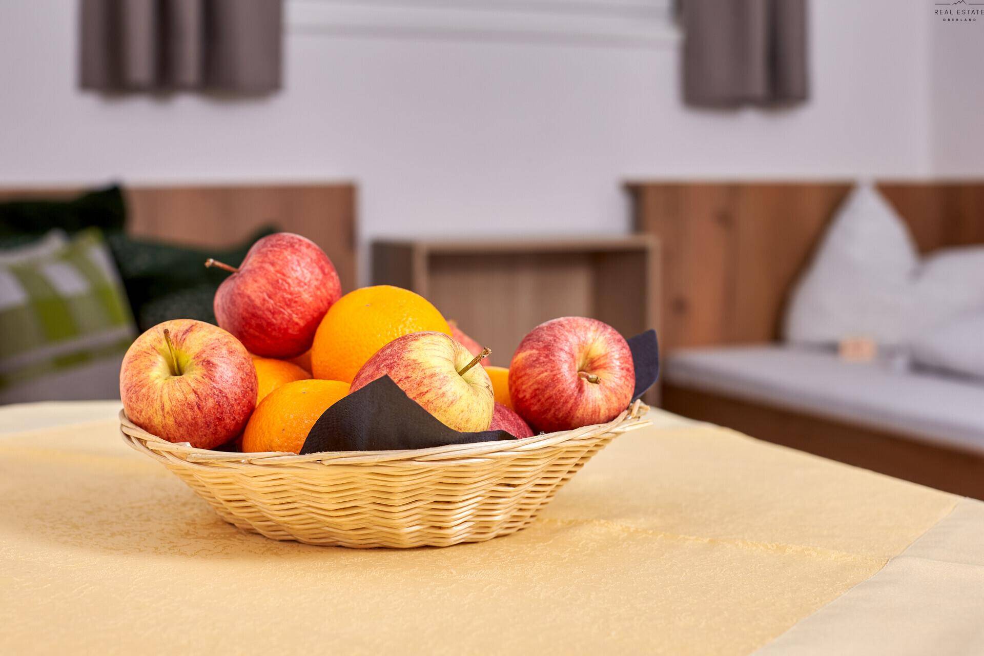Korb mit frischem Obst auf einem Tisch in einem hellen Zimmer mit Holzelementen.