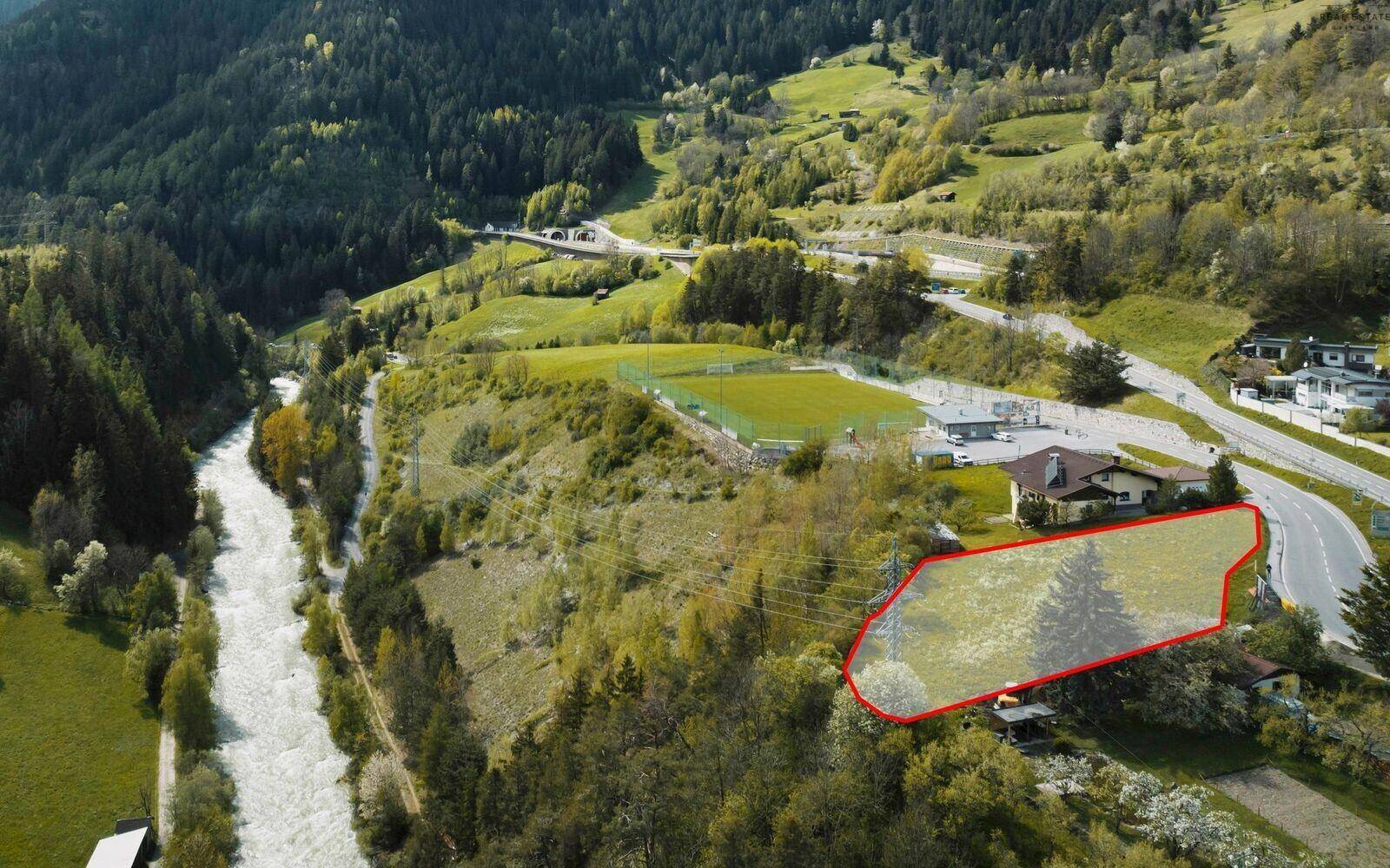 Luftaufnahme eines Grundstücks mit roter Umrandung, angrenzend an einen Fluss und einen Sportplatz.