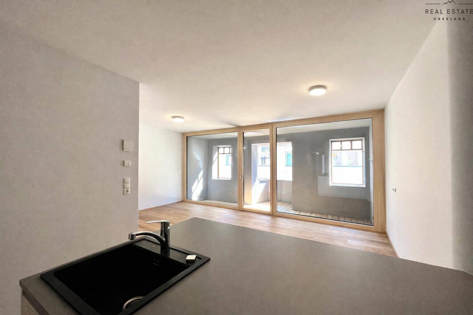 Blick vom Küchenbereich auf den hellen Wohnraum mit großen Fenstern und Zugang zum Außenbereich.