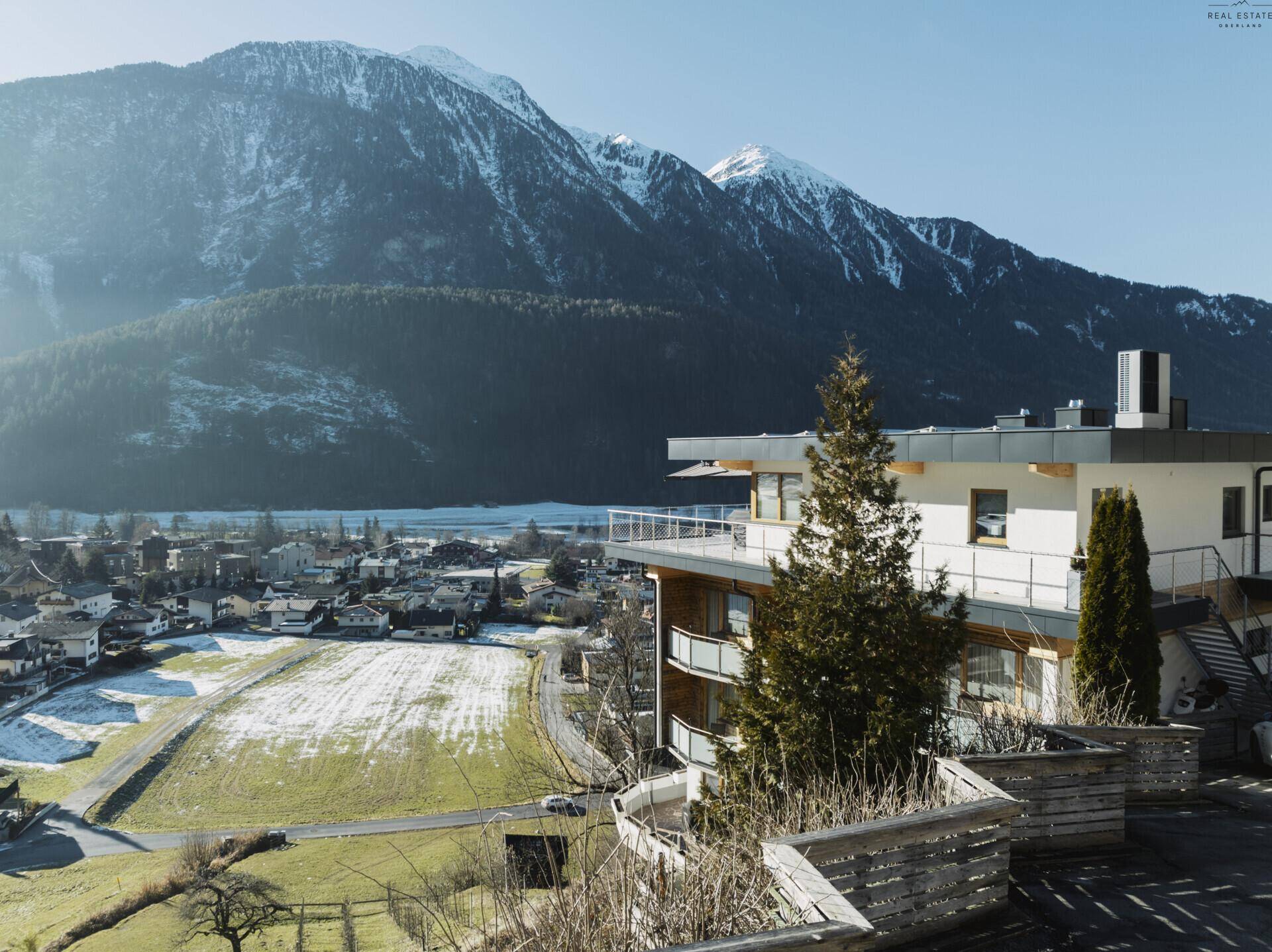 Modernes Gebäude mit Balkonen in einer verschneiten Berglandschaft mit weitem Blick.