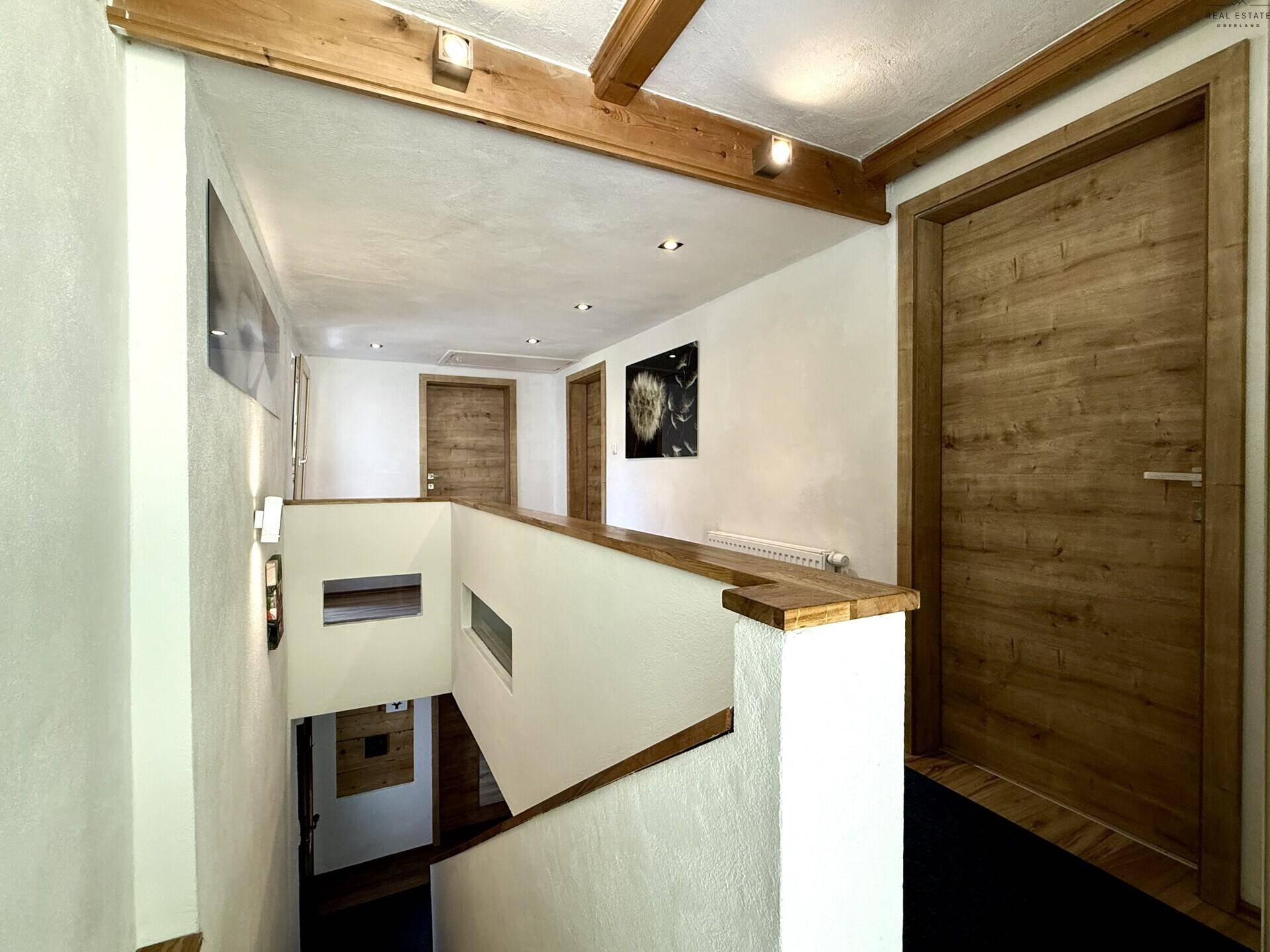 Heller Flur im Obergeschoss mit Holzgeländer und Holzbalken an der Decke, führt zu weiteren Zimmern.