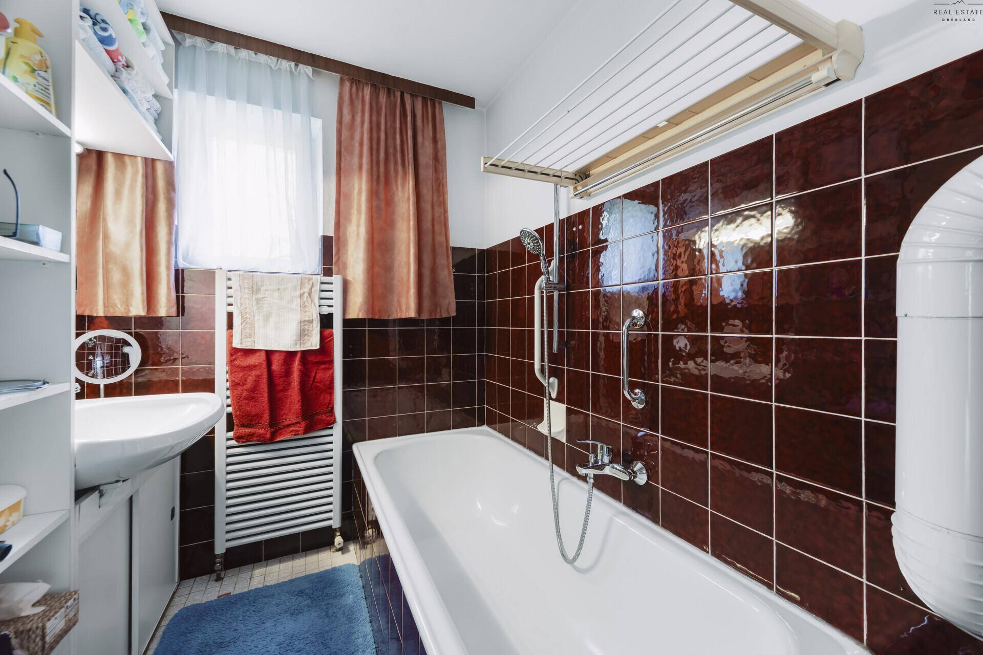 Badezimmer mit Badewanne, Waschbecken und braunen Fliesen, ausgestattet mit Handtuchhalter.