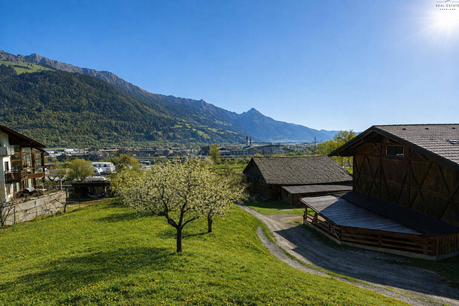 Weitläufige Landschaft mit grünen Hügeln, alten Gebäuden und einem Panoramablick auf die Berge.