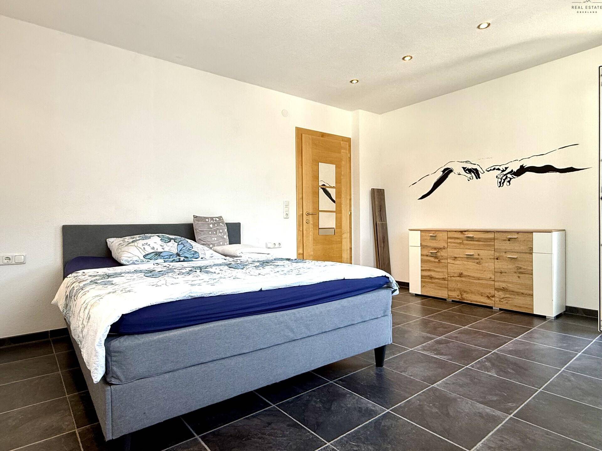 Schlafzimmer mit dunklem Fliesenboden, Doppelbett und einem modernen Sideboard aus Holz.